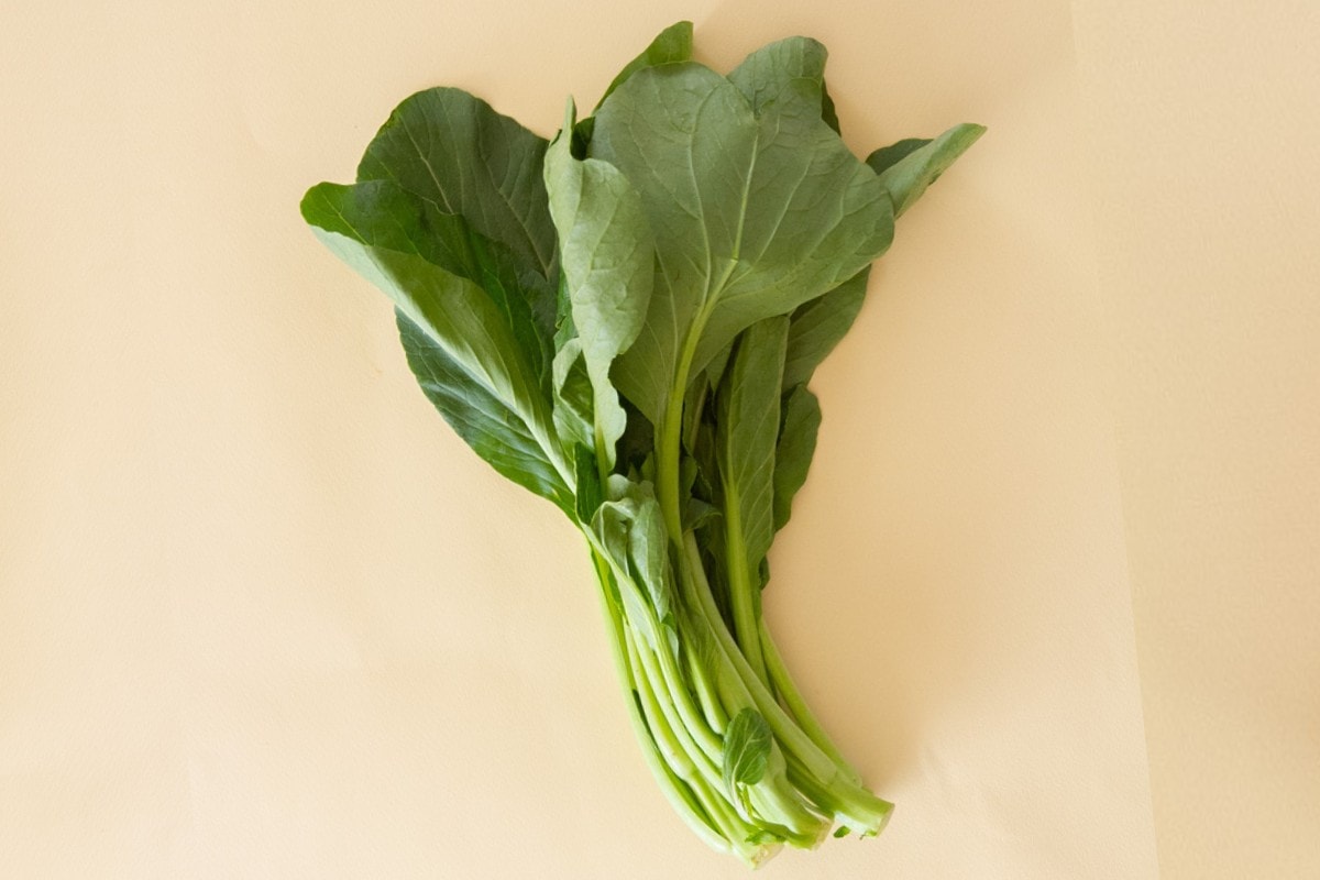 A small bunch of yu choy over a pastel yellow background.