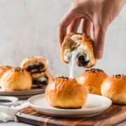 A mochi red bean bun cut in half on a white plate with a hand holding one half up to show the mochi pull.