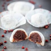 A red bean mochi cut in half on a black surface with more in the background and dried red beans sprinkled around.