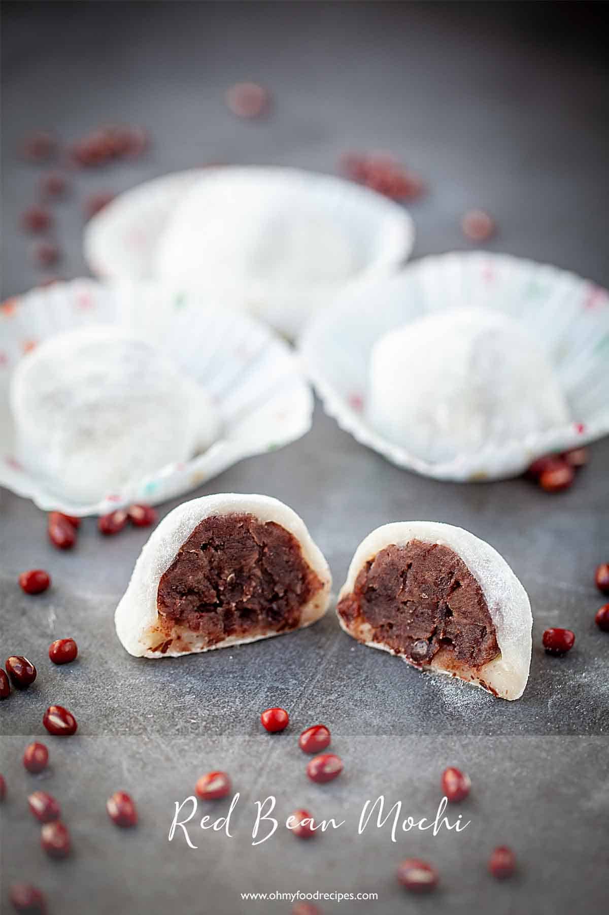 A red bean mochi cut in half on a black surface with more in the background and dried red beans sprinkled around.