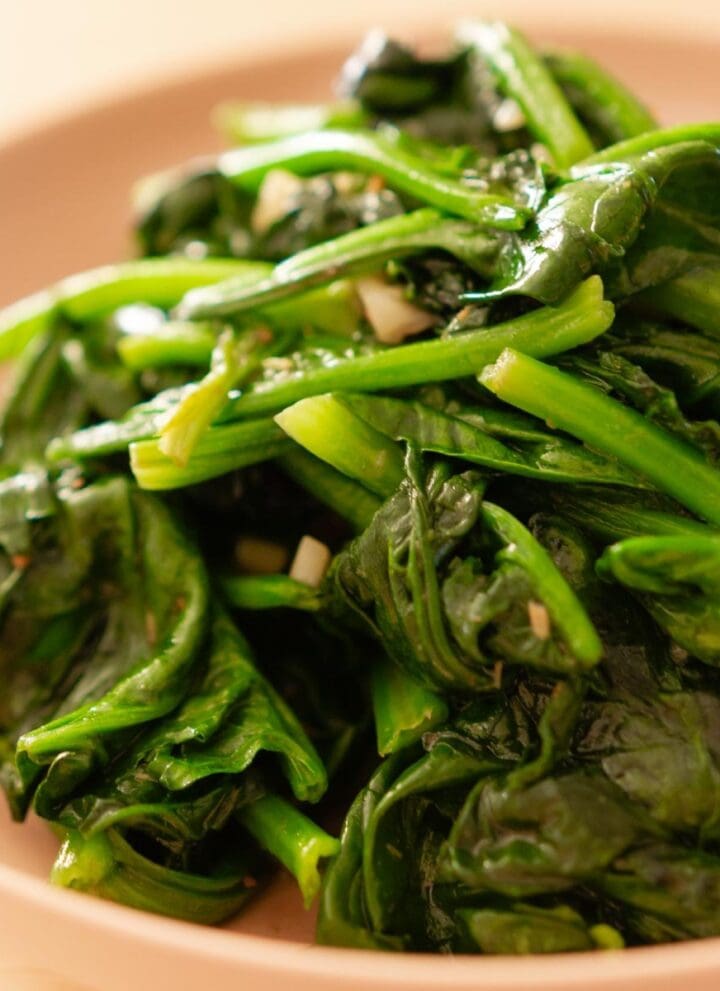 Stir-fried spinach with garlic in a pink serving plate.