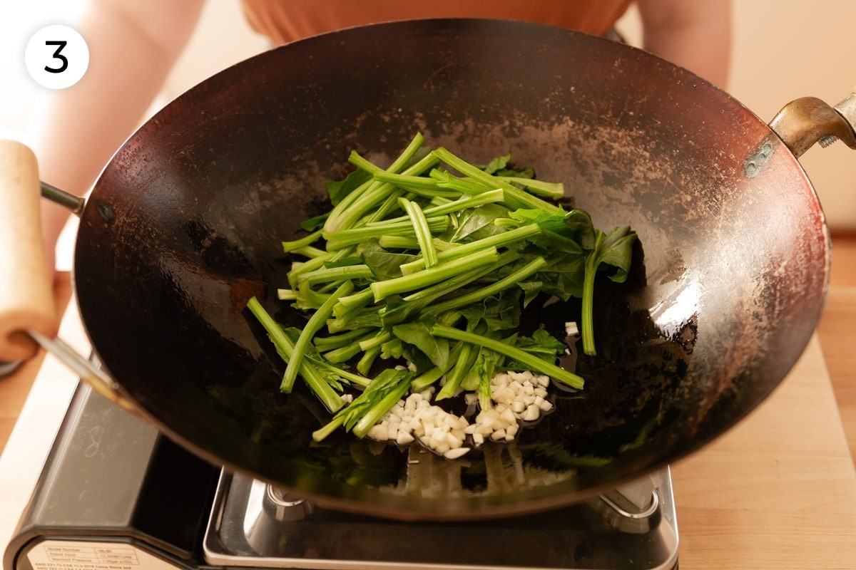 Top down view of cut Taiwan spinach stems and roughly minced garlic in a heated wok, labeled with a circled number "3."