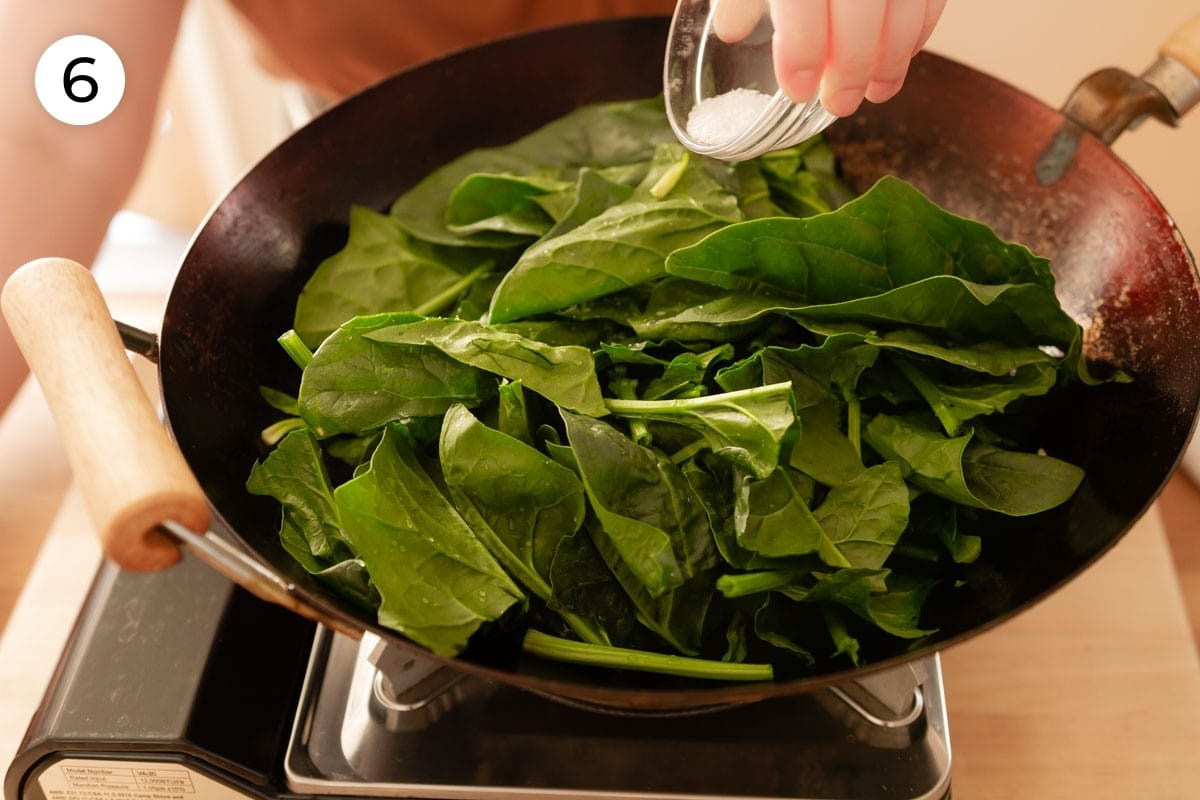 Cindy pouring salt over the spinach in the wok, labeled with a circled number "6."