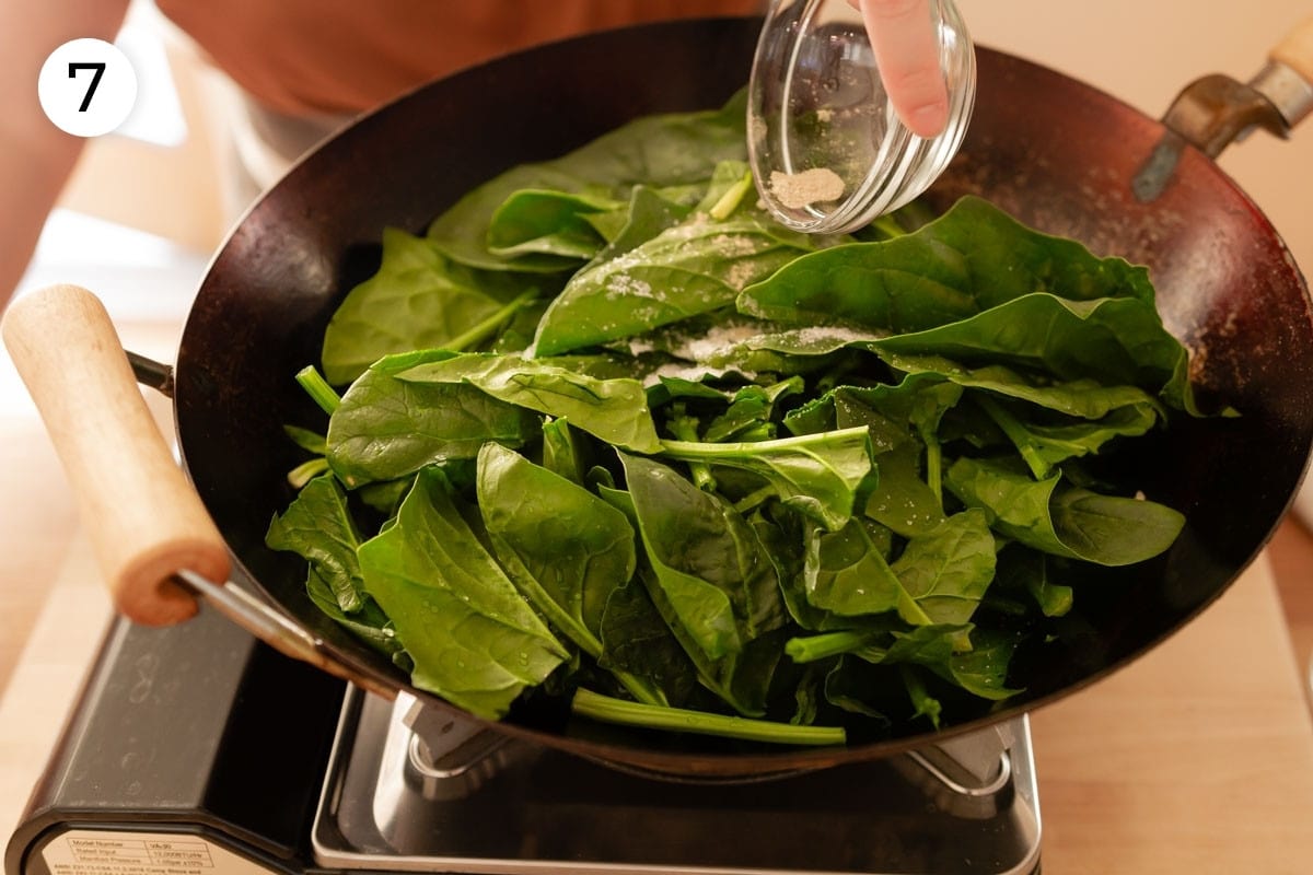 Cindy pouring ground white pepper over the spinach in the wok, labeled with a circled number "7."