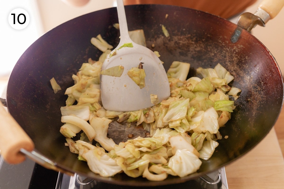 Cindy using a metal spatula to stir the cooked cabbage and showing the bottom of the wok is mostly dry to show how the liquid has cooked off, labeled with a circled number "10."