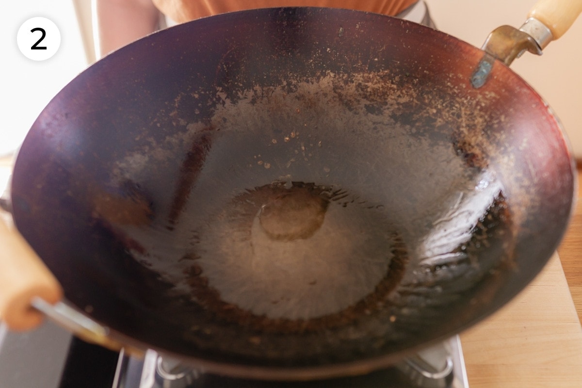 Top down view of a heated wok with canola oil in it (showing the ripples in the oil), labeled with a circled number "2."
