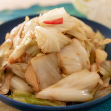 Stir-fried Taiwanese cabbage with minced garlic, thai chili, and sauce in a blue serving plate over a patterned textile.