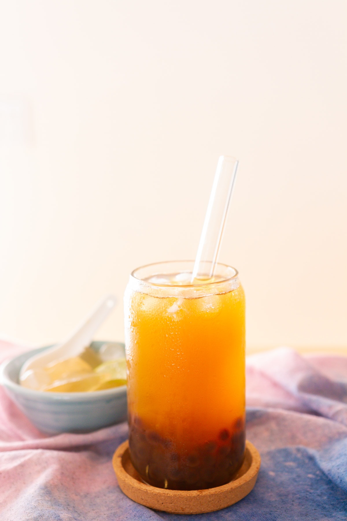 A glass of bubble tea with aiyu as a topping and a boba straw in front of a bowl of scooped traditional aiyu.