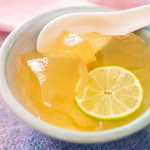 Scoops of aiyu jelly in a blue bowl with a white porcelain spoon, topped with lime juice, honey, and a slice of lime.