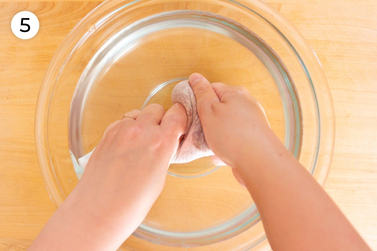 Recipe step 5: Cindy using both hands to rub the aiyu seed filled mesh bag in a large bowl of clear hard (mineral) water.