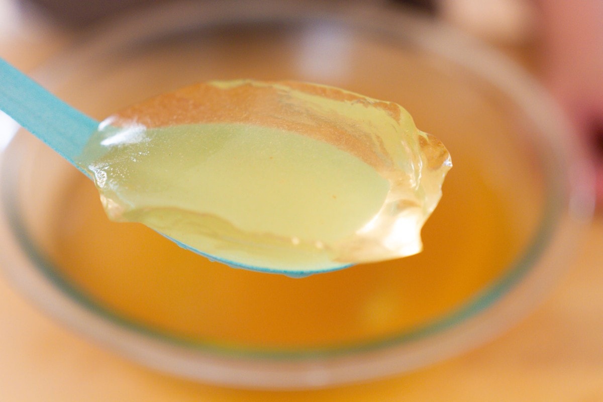 A close up view of fresh aiyu jelly in a turquoise Asian soup spoon to show the translucent, pale golden color and texture.