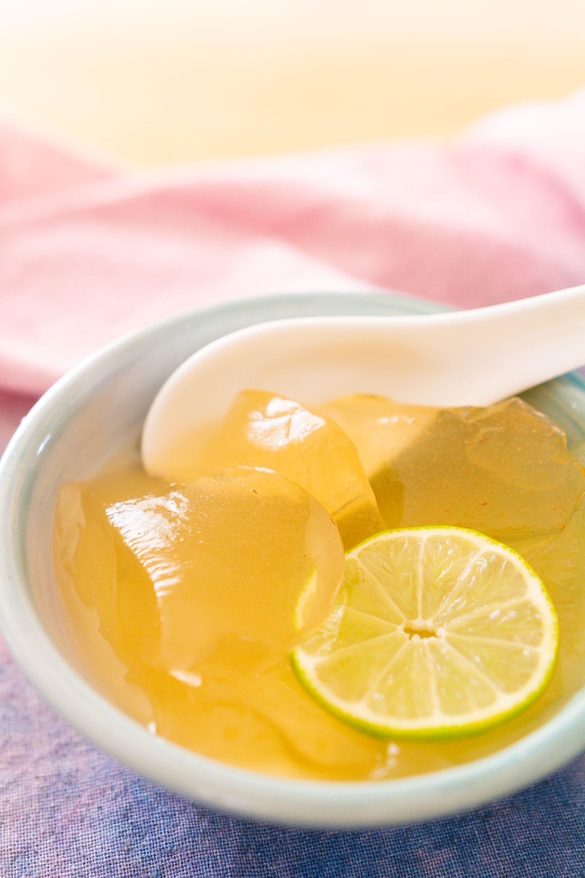 Scoops of aiyu jelly in a blue bowl with a white porcelain spoon, topped with lime juice, honey, and a slice of lime.