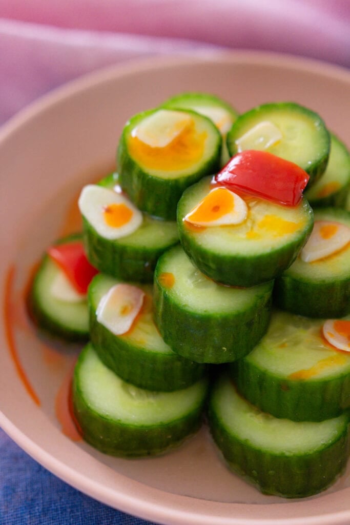 Dressed Taiwanese Din Tai Fung cucumber salad plated and topped with garlic slices, red chili pepper slices, and chili oil.