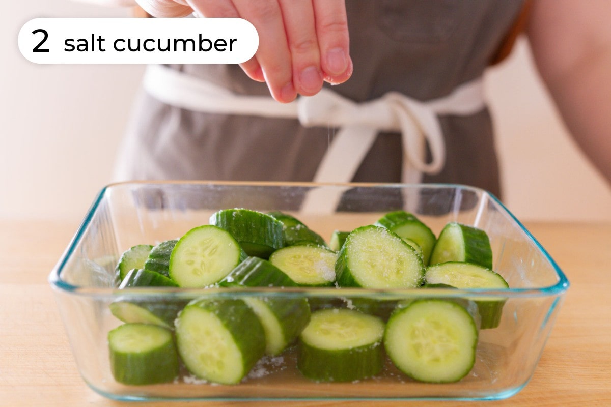 Recipe step 2 - salt cucumber: Cindy sprinkling Diamond Crystal kosher salt over the cut cucumbers in a rectangle glass dish.