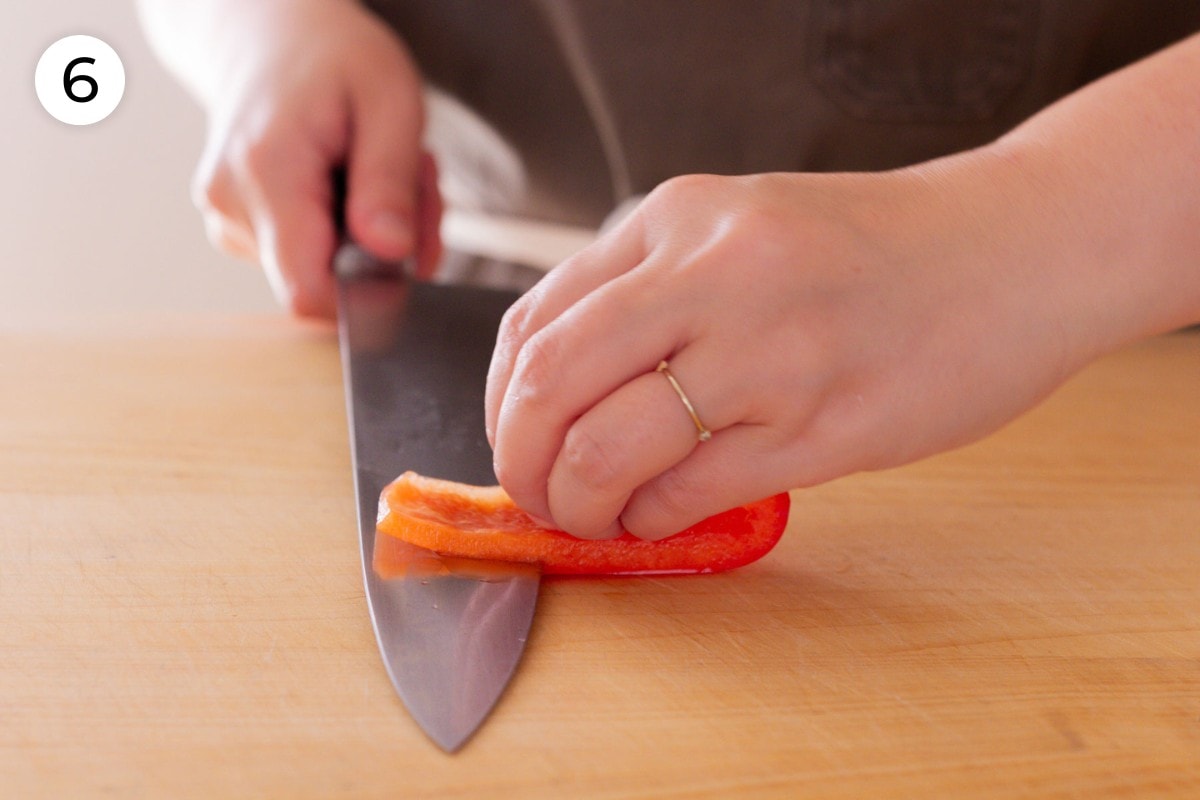 Recipe step 6 (optional): Cindy holding a slice of red bell pepper flat on a cutting board and slicing it close to the skin with a chefs knife held parallel to the cutting board.