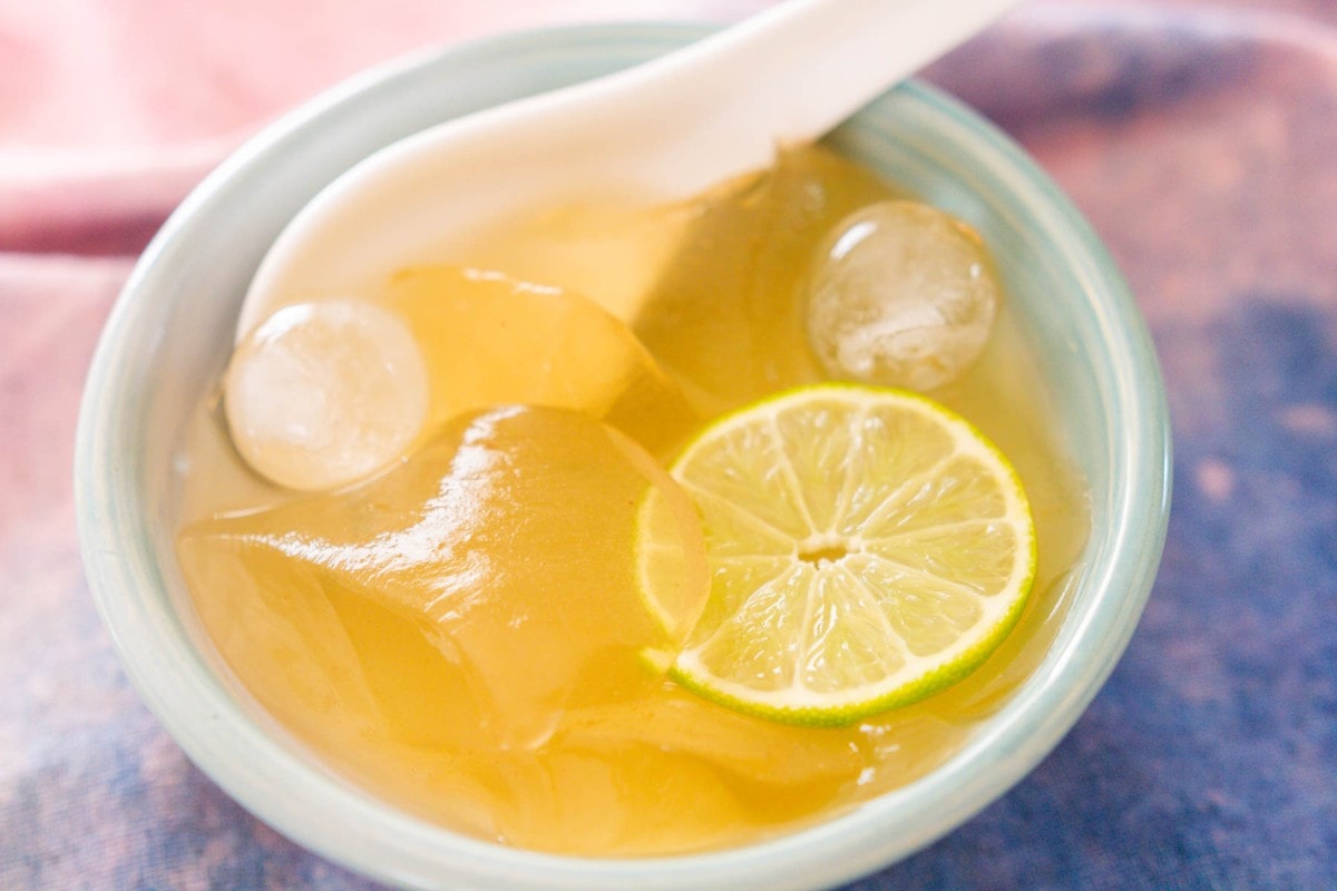 Scoops of aiyu in a blue bowl with a white porcelain spoon, topped with lime juice, honey, ice, and a thin slice of lime.