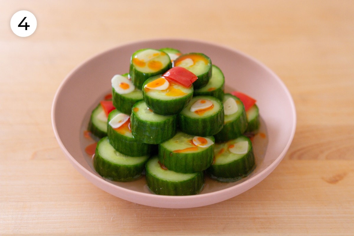 Din Tai Fung cucumber salad recipe plating step 4: cucumber slices stacked like a circular pyramid in 4 layers and topped with thinly sliced garlic and red chili pepper, dressing, and Chinese red chili oil.