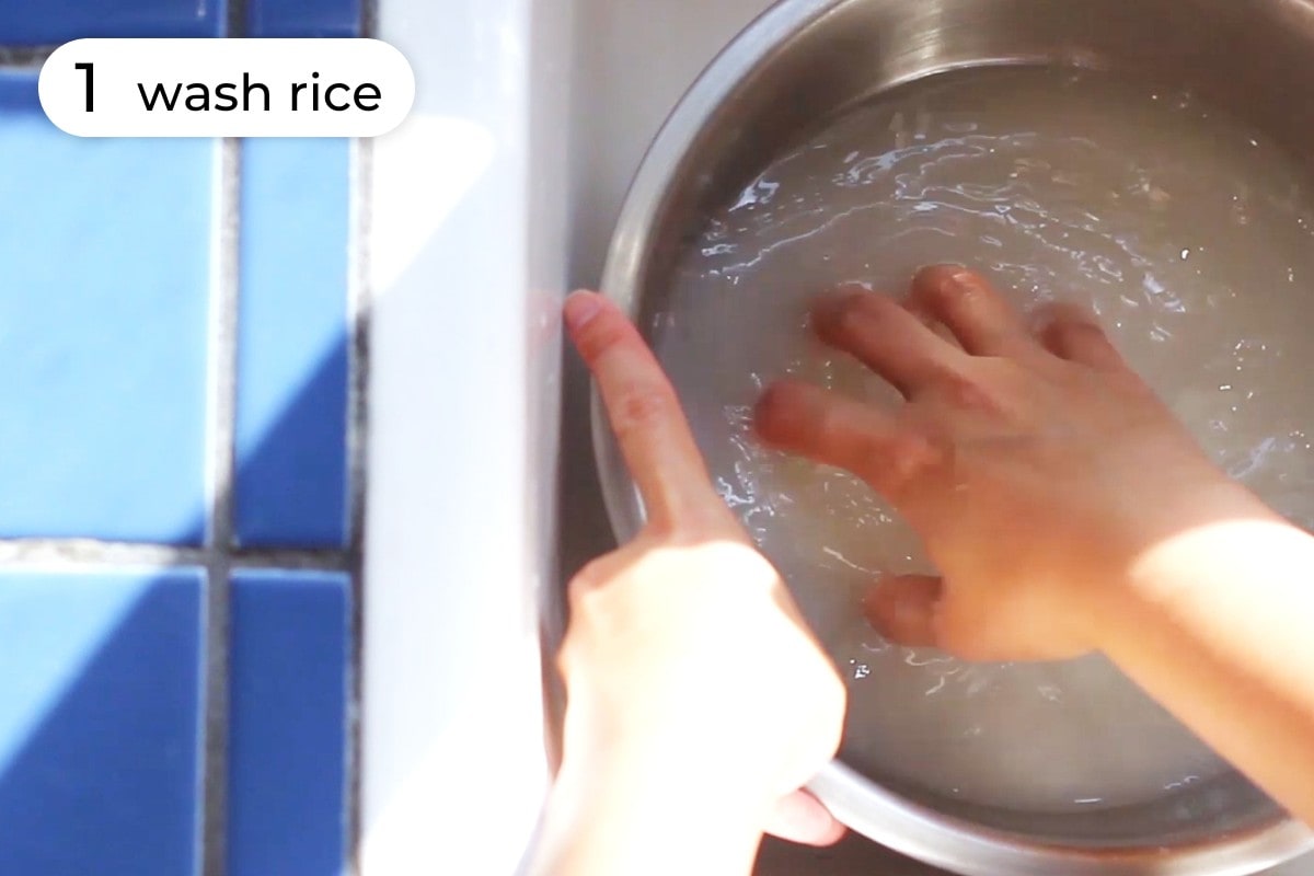 Recipe step 1: Cindy holding a medium mixing bowl in the sink with one hand and stirring rice with clean water inside.