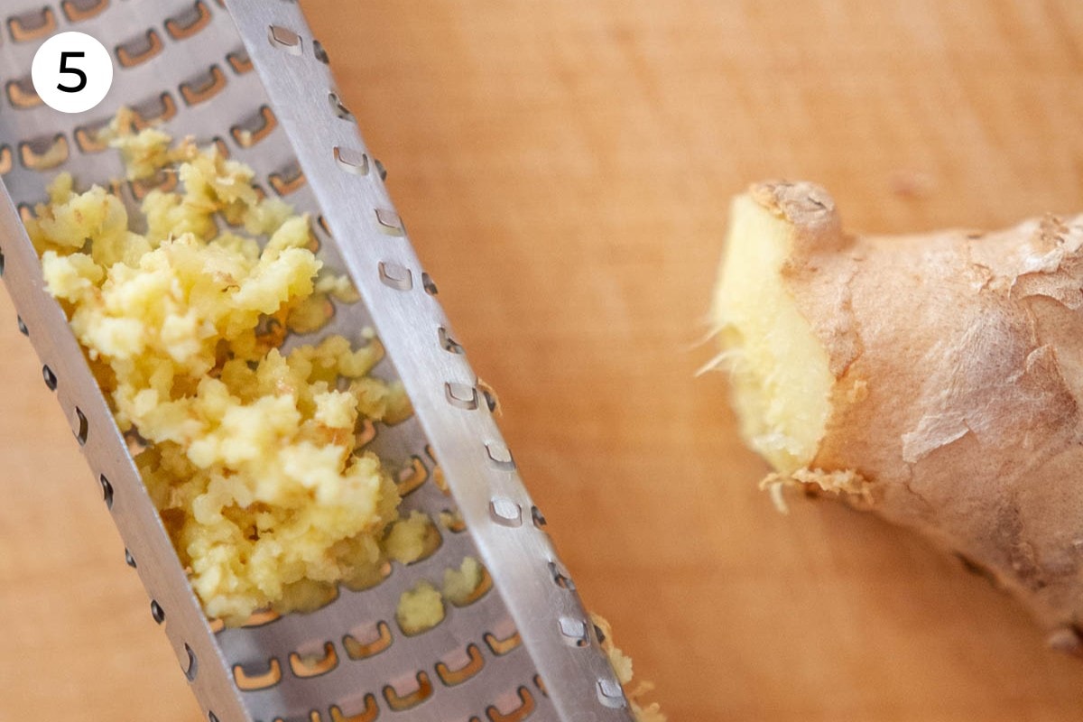 Recipe step 5: A close up view of grated ginger on the underside of a microplane, next to a piece of fresh ginger.