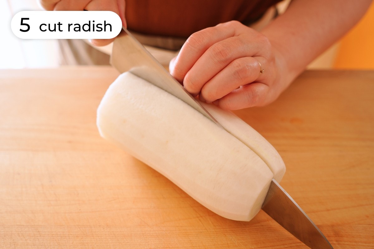 Recipe step 5: Cindy cutting a 6-inch long piece of peeled daikon radish in half lengthwise.