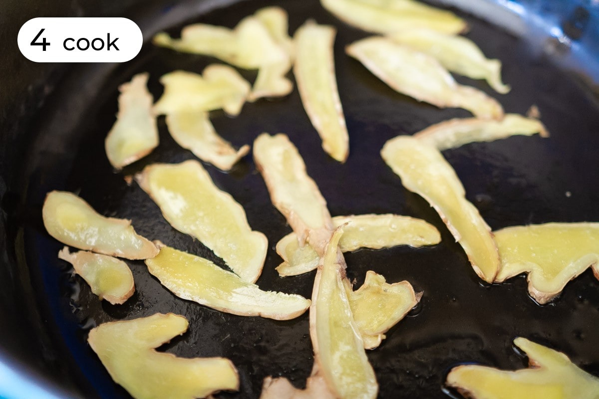 Recipe step 4 - cook: Thin slices of ginger spread out in a large dutch oven with cooking oil.