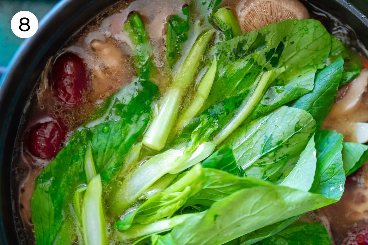 Recipe step 8: Top view of yu choy greens added to the top of the cooked soup in a pot.