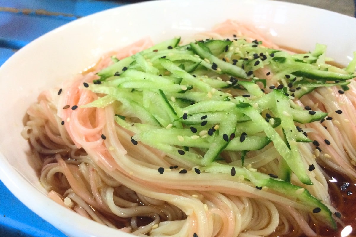 A bowl of Taiwan longevity noodles coated in sesame oil sauce and topped with shredded cucumber and toasted sesame seeds.
