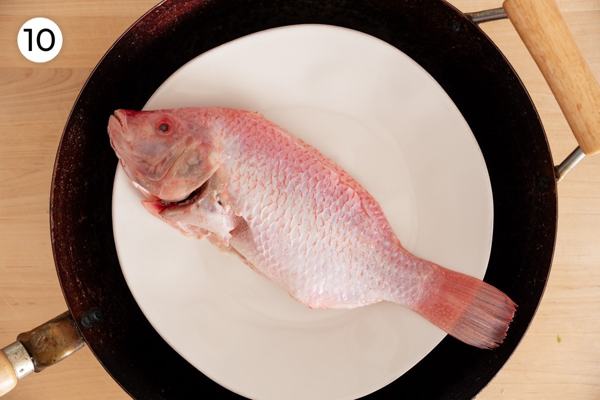 Recipe step 10: Top-down view of the cleaned whole fish on a white plate in a 14-inch wok, sitting on the steamer tray.