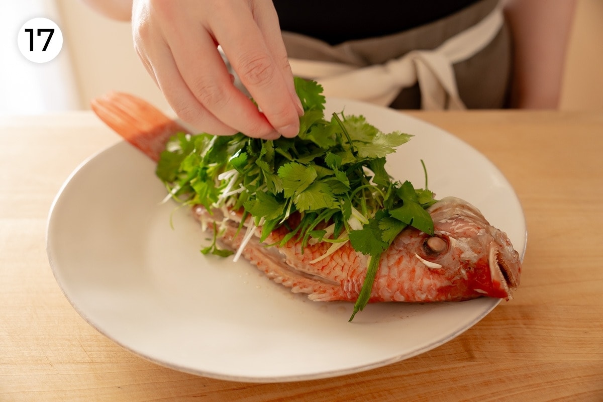 Recipe step 17: Cindy topping the freshly steamed fish with fresh ginger, scallions, and cilantro.