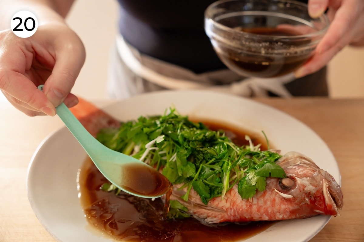 Recipe step 20: Cindy using a deep soup spoon to dish the sauce onto the plate around the fish.