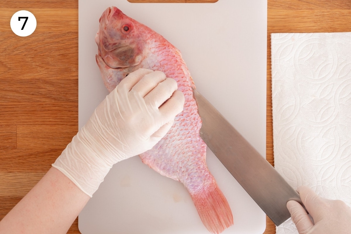 Recipe step 7: The fish on a non-porous cutting board with the tail pointed towards Cindy while she uses one smooth slicing motion to cut along the edge of the top fin about 1½-inch deep (parallel to the cutting board) from the head to tail using the backbone as a guide.
