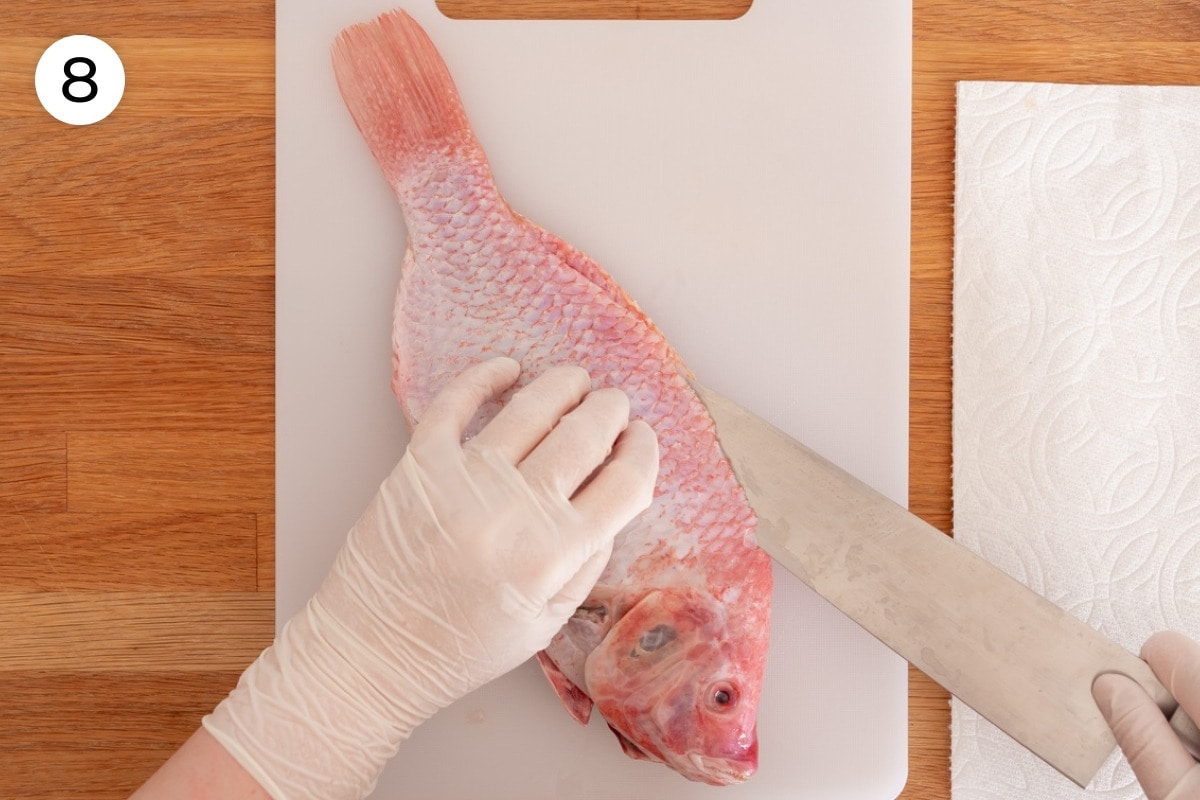 Recipe step 8: The fish flipped over on the cutting board with the head now pointed towards Cindy while she uses one smooth slicing motion to cut along the edge of the top fin about 1½-inch deep (parallel to the cutting board) from the tail to head using the backbone as a guide.