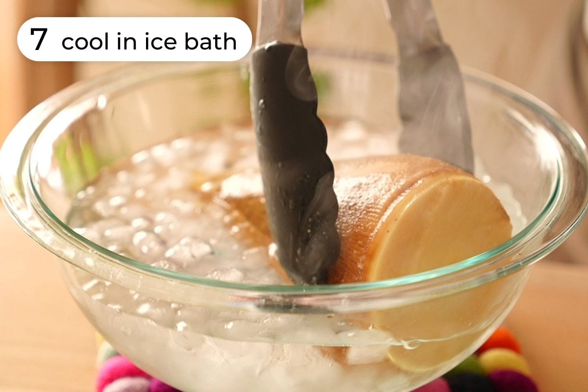 Recipe step 7 - Tongs transferring a steaming cooked bamboo shoot into an ice bath in a large mixing bowl.