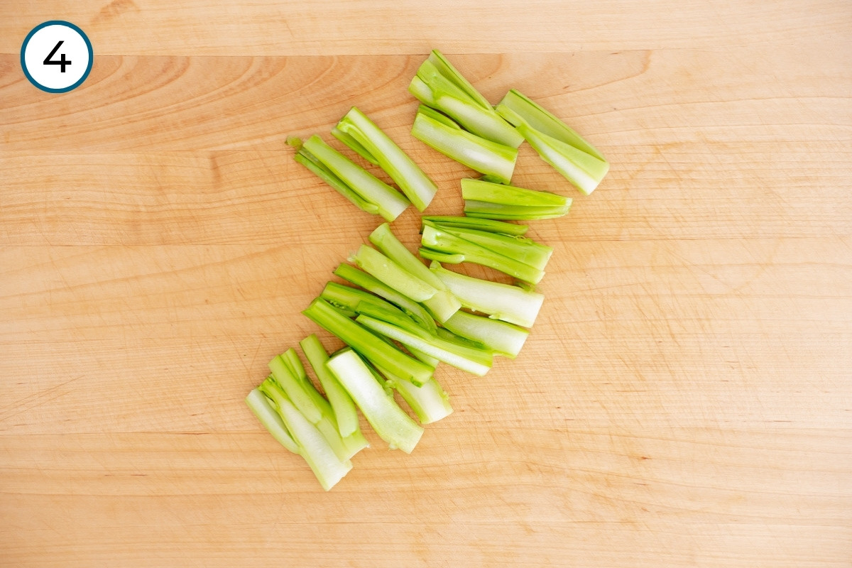 How to Cut Step 4 – Choy sum stems that have been cut in half lengthwise spread out on a wooden cutting board.