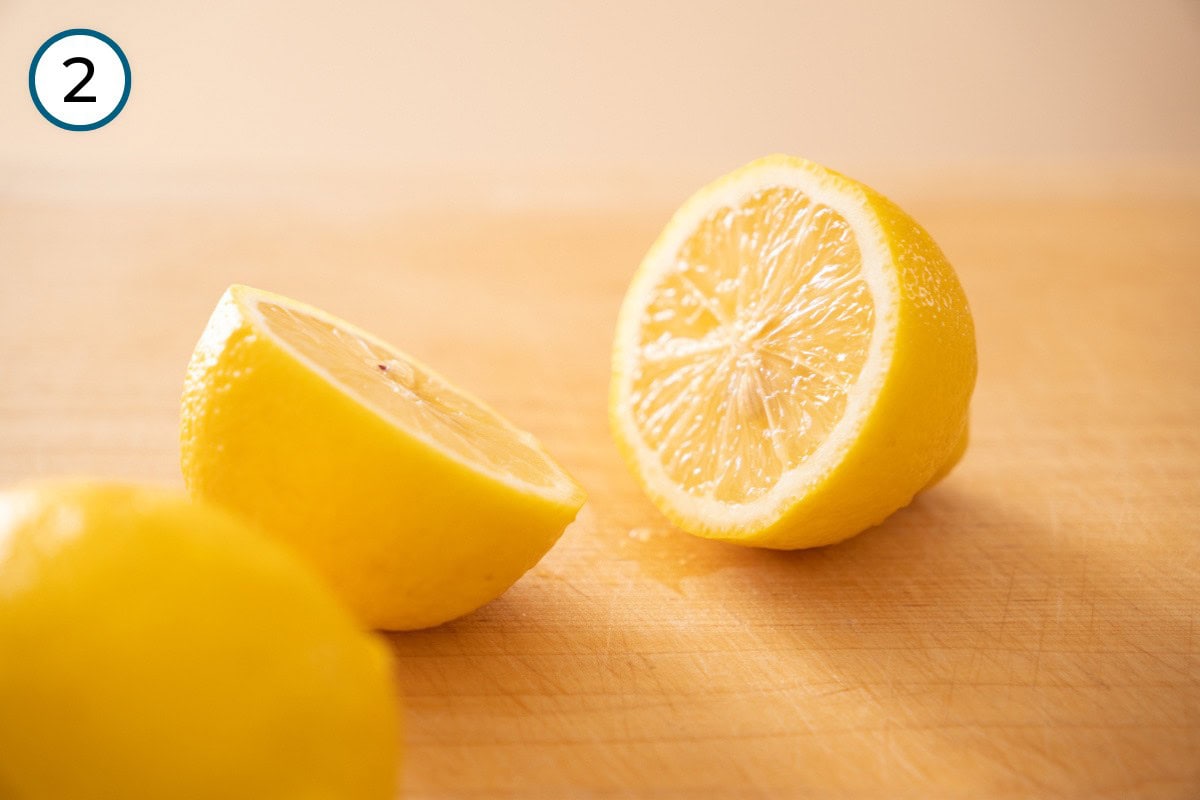 Recipe Step 2 – Two lemon halves and a whole lemon on a wooden surface.