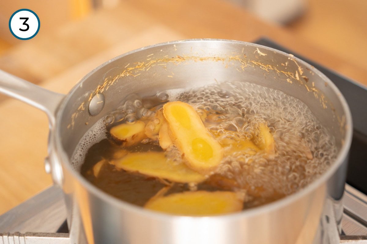 Recipe Step 3 – Pot of water boiling with slices of ginger on a stove.