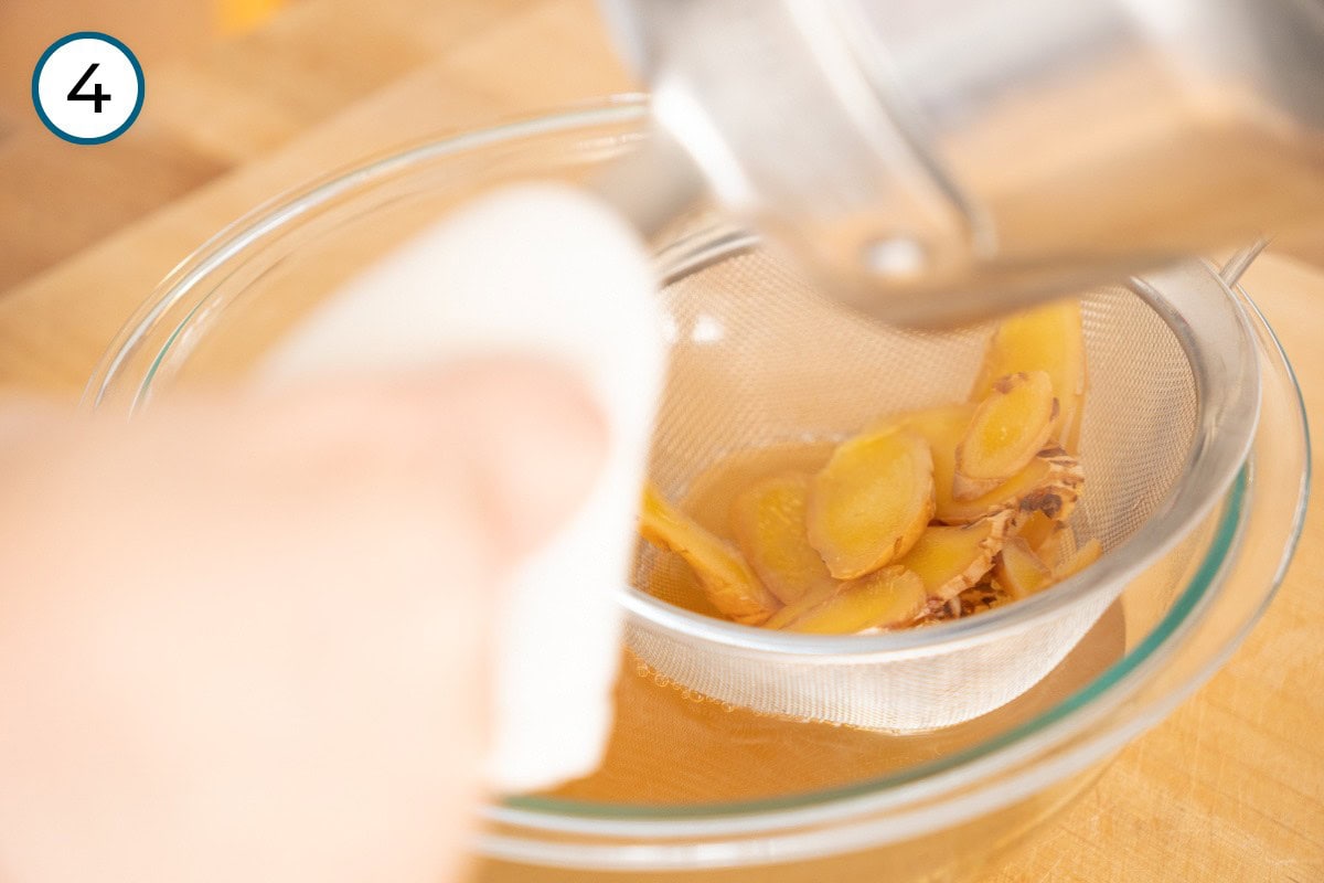 Recipe Step 4 – Cindy pouring the golden ginger water through a strainer into a large mixing bowl, with the sliced ginger caught inside the strainer.