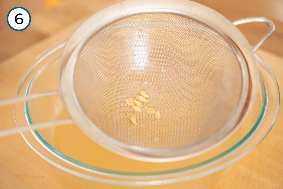 Recipe Step 6 – A mesh strainer with lemon seeds sits over a glass bowl containing ginger water and lemon juice.