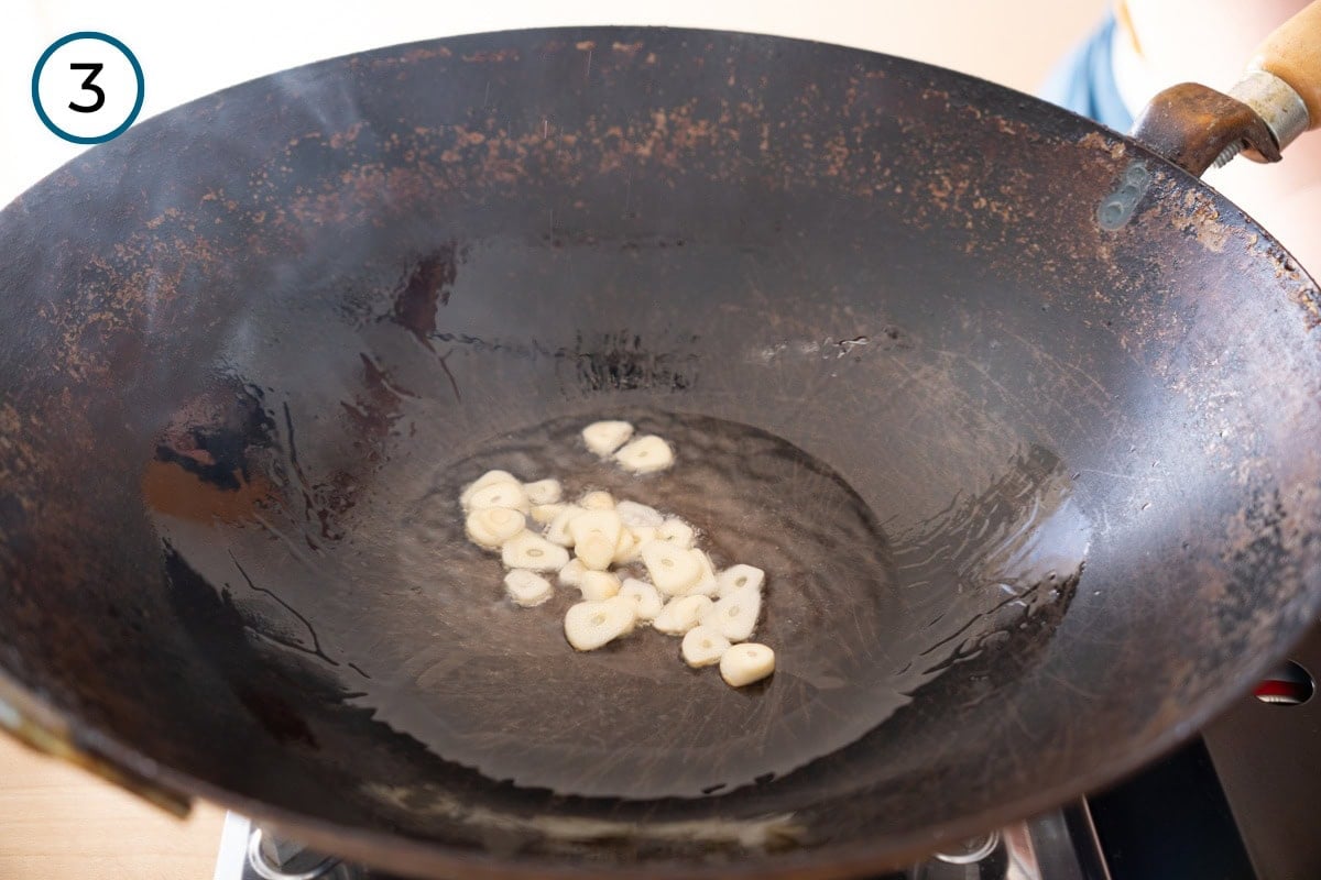 Stir-fried pea shoots step 3 - Sizzling slices of garlic in a thin layer of hot oil in a wok.
