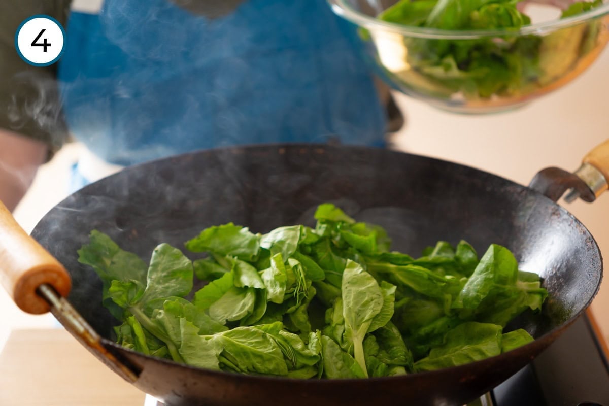 Stir-fried pea shoots step 4 - Washed pea shoots being added to a hot wok on a stove.