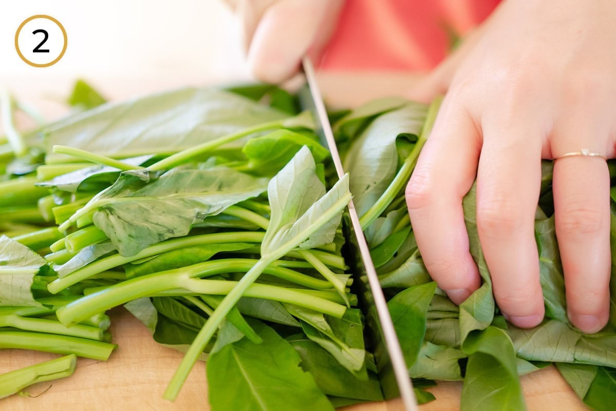 Cut morning glory step 2 - Cindy cutting the morning glory leaves into shorter pieces on a wooden board with a chef's knife.