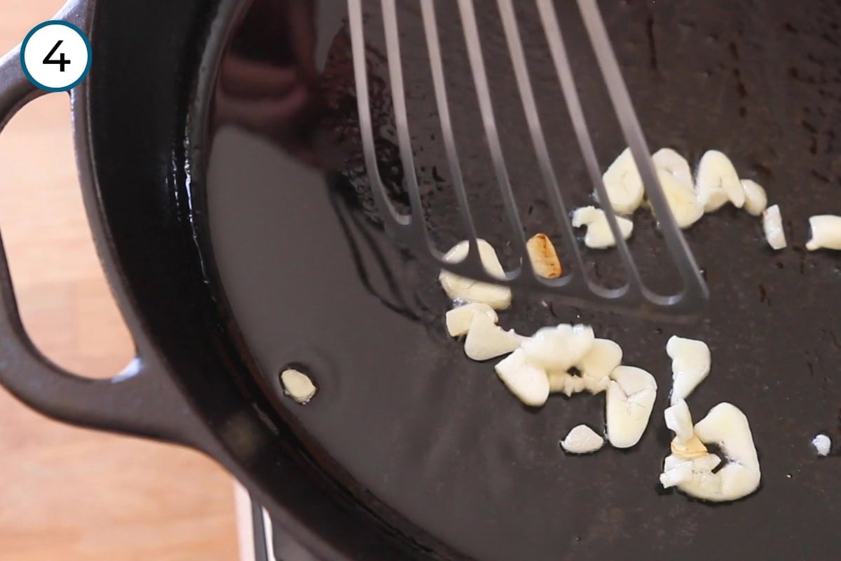 Stir-fried morning glory step 4 - Cindy stirring the garlic with a metal fish spatula in the cast iron pan.