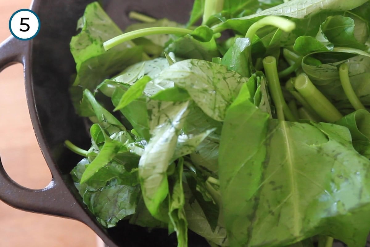 Stir-fried morning glory step 5 - Washed morning glory added to a hot cast iron pan, stems first then topped with the leaves.